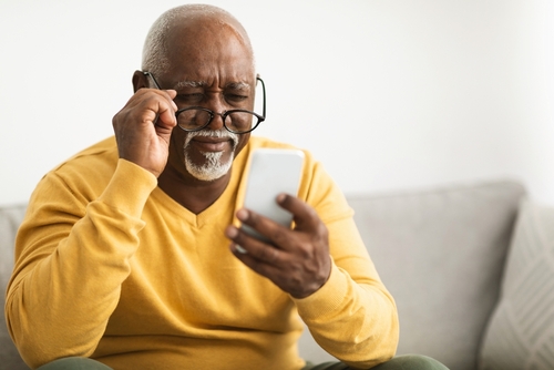Senior man squinting at phone with glasses, facing reading challenges before treatment