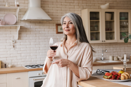 Mature woman savoring red wine in modern kitchen, appreciating details with improved vision post-lens implant