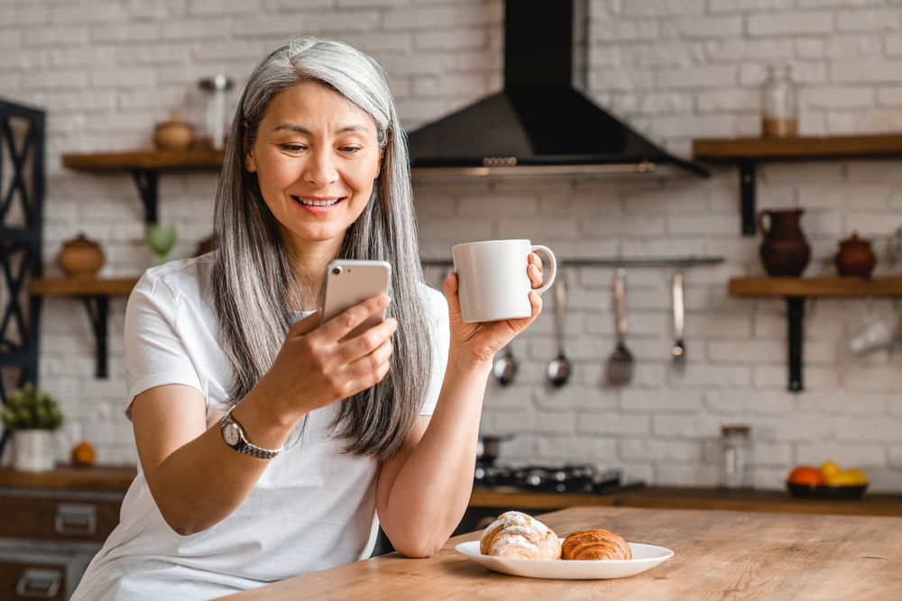 Senior woman smiling while using smartphone and enjoying coffee, clear vision post-cataract surgery