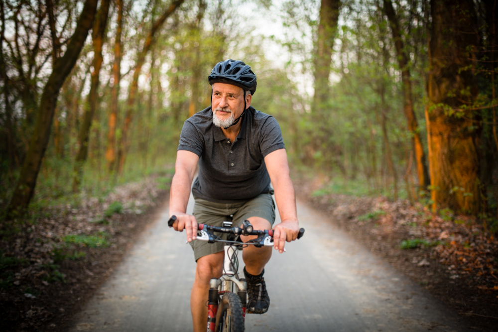 Enthusiastic senior man biking through sunny park path, joyful mobility with corrected vision