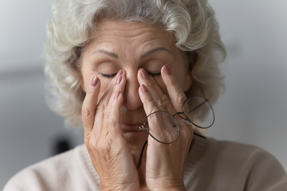Elderly woman rubbing eyes while wearing glasses, showing eye strain from vision impairment
