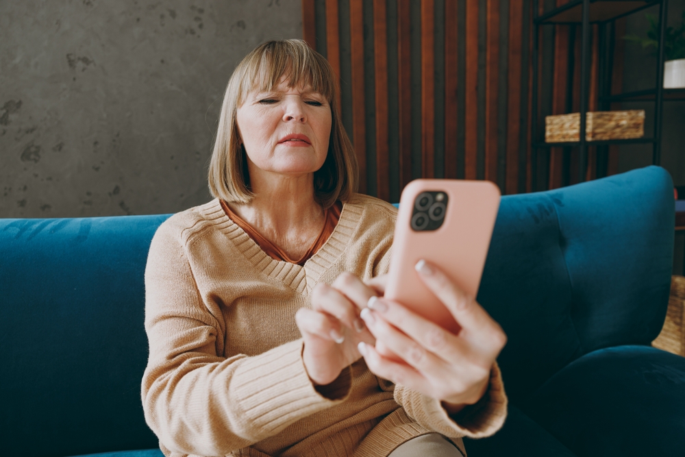 Senior woman squinting at smartphone screen indoors, illustrating cataract-related reading difficulties