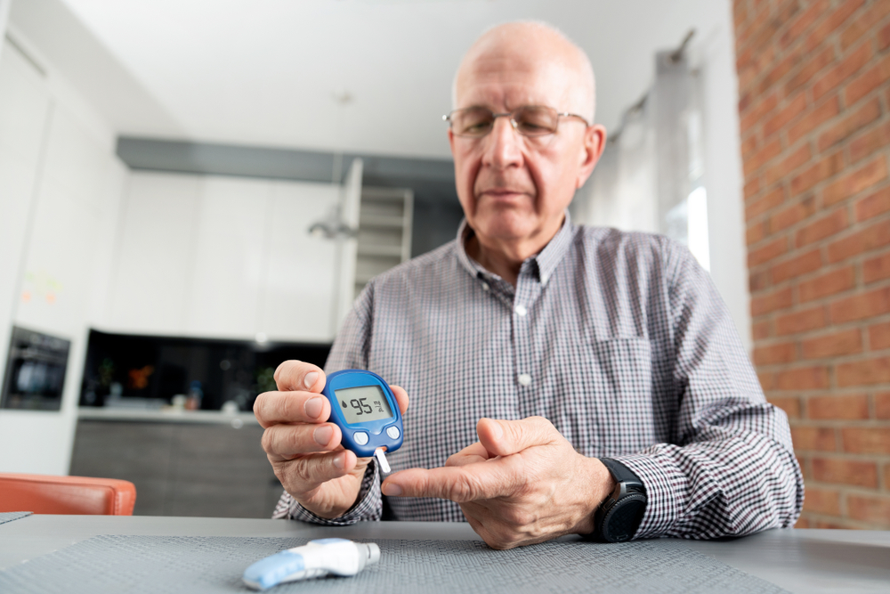 Senior man monitoring blood sugar levels at kitchen table, diabetes management to prevent retinopathy complications