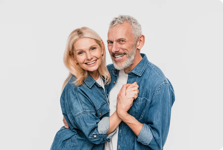 Smiling elderly couple embracing in denim – joyful clear vision with EDOF lenses post-cataract surgery.
