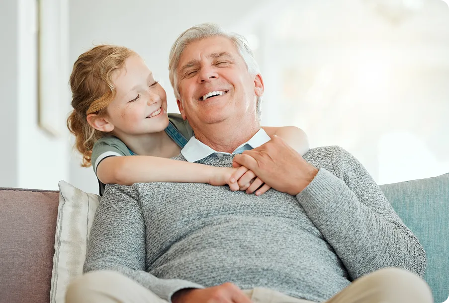 Grandfather hugging granddaughter on sofa – family warmth with post-surgery clear vision.
