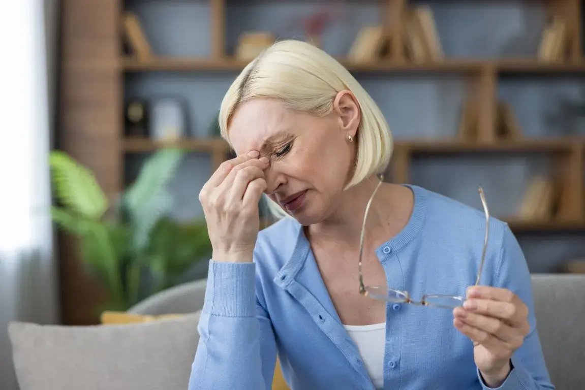 Adult woman holding her eyeglasses and rubbing one eye because of vision discomfort.